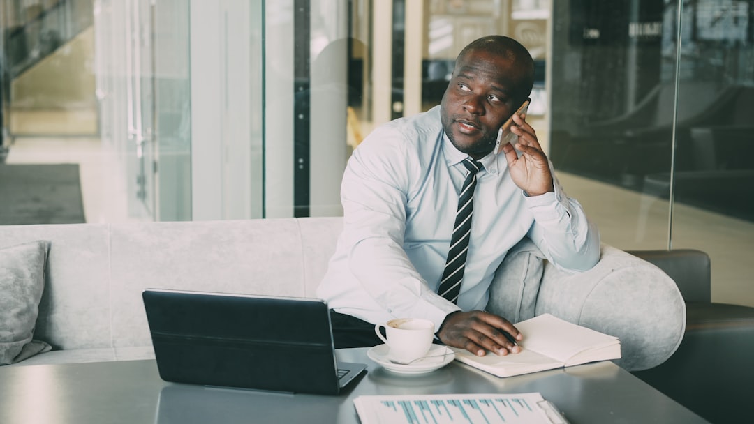 Man in suit talking on phone with laptop and book.